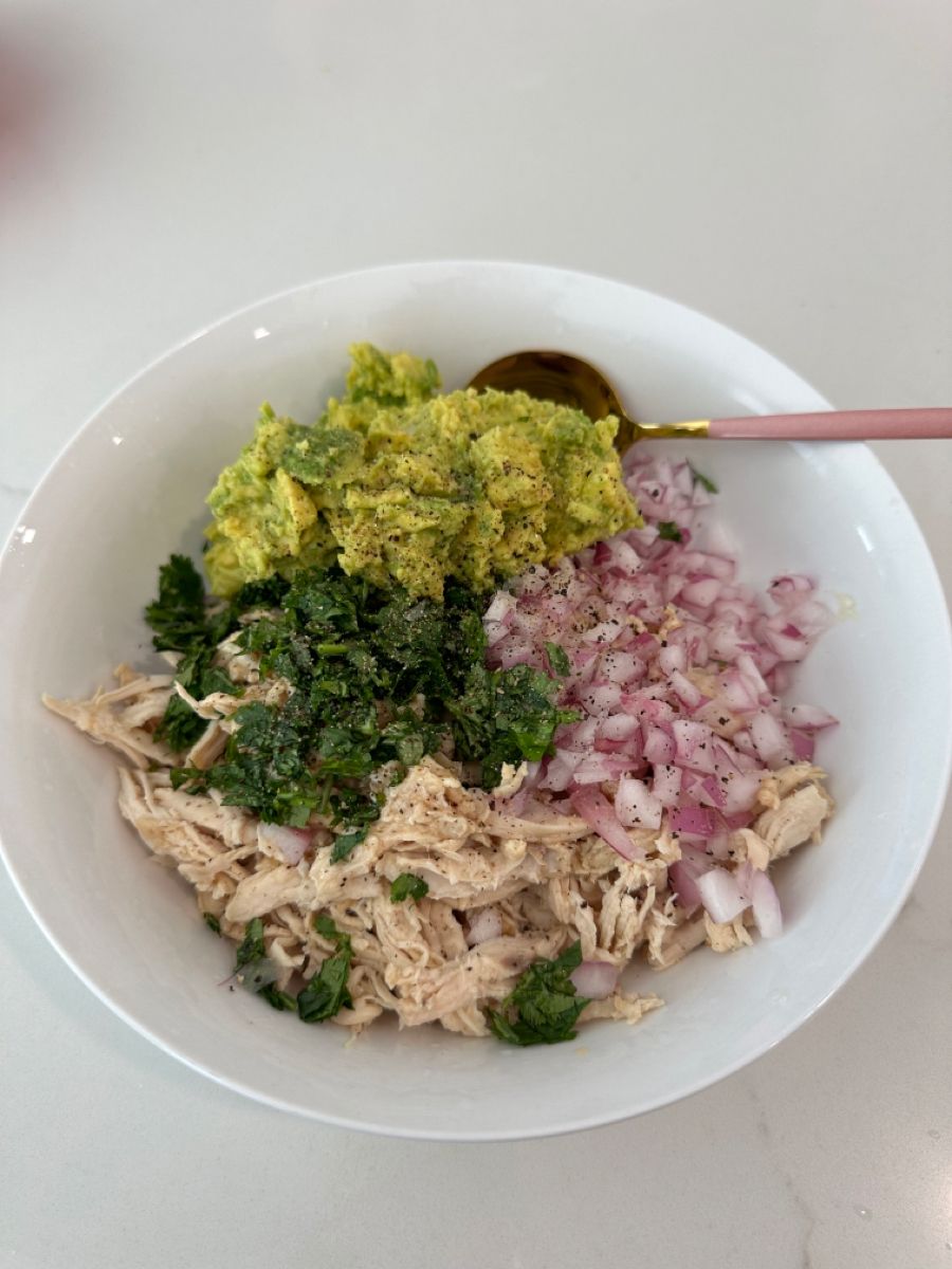Bowl of shredded chicken, avocado, herbs and red onion